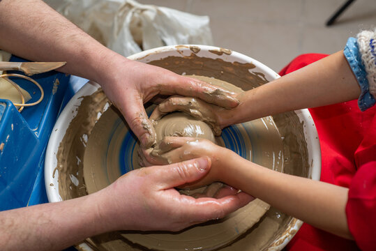 Faceless Master teaches a child to work with clay on a potter's wheel