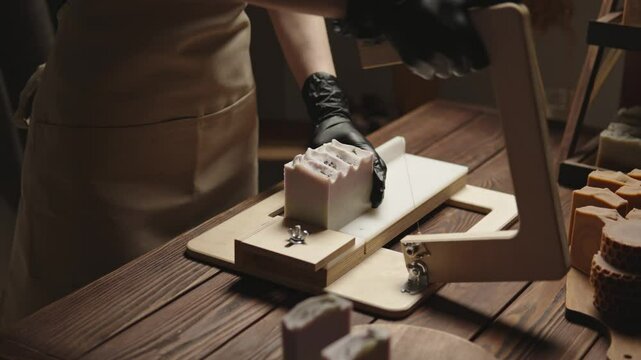 A woman master soap maker cuts handmade lavender soap on a wooden string cutter. Home production of natural cosmetics