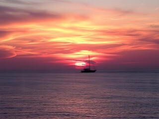 Fototapeta premium Solitude at Sunset: A solitary sailboat silhouetted against a breathtaking sunset, as fiery hues paint the sky in a dramatic display of nature's artistry.