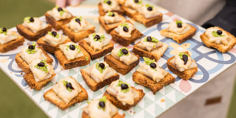 A waiter holds a tray of smoked cod toast, covered with mayonnaise and a drop of vinegar cream