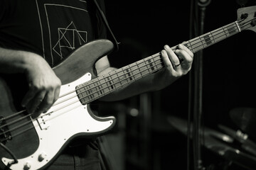 A close-up shot of a musician playing a bass guitar. The focus is on the strings and the musician's...