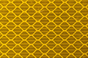 Macro texture of a reflective yellow, retro-reflective material, on a traffic sign, made up of a repetitive honeycomb-shaped pattern