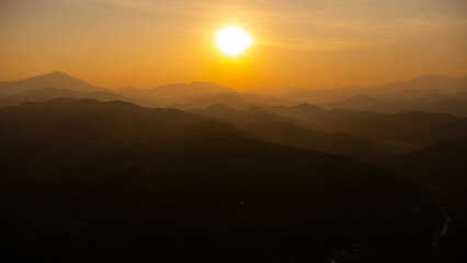 Beautiful sunset in the winter mountains. The setting sun shines down on a serene mountain landscape covered with tropical trees in the evening.