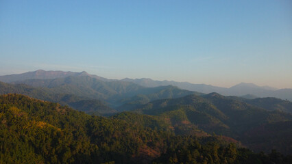 Beautiful sunrise on the mountain with fog in winter. The sun shines down on a serene mountain landscape covered with tropical trees in the early morning.