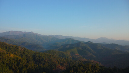 Beautiful sunrise on the mountain with fog in winter. The sun shines down on a serene mountain landscape covered with tropical trees in the early morning.