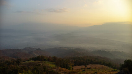 Beautiful sunrise on the mountain with fog in winter. The sun shines down on a serene mountain landscape covered with tropical trees in the early morning.