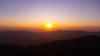 Beautiful sunset in the winter mountains. The setting sun shines down on a serene mountain landscape covered with tropical trees in the evening.