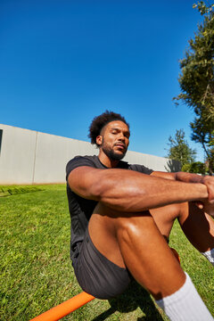 Cheerful black man sitting on parallel bars in park in sunny day