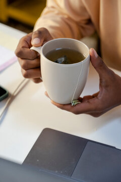 Crop of anonymous man's hands holding cup of tea in office