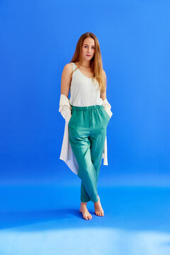 Slim woman in blue dress standing in blue studio and looking at camera