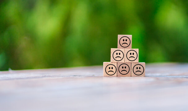 Wooden blocks with sad faces stacked in a pyramid shape on a blurred green background.  Sadness, depression, or negative emotions concept. ideal for mental health or emotional well-being concepts.