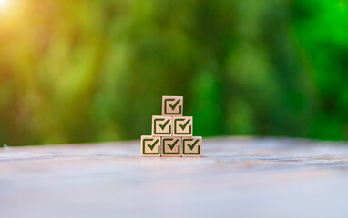 Wooden blocks arranged in pyramid shape displaying green checkmark symbols against blurred nature background. Business concept of success, achievement, task completion, and goal accomplishment.