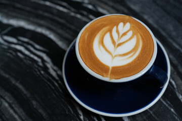Latte art coffee in blue cup on black table.