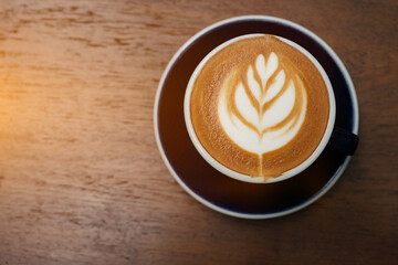Latte art on a coffee cup on a wooden table in the warm sunlight.