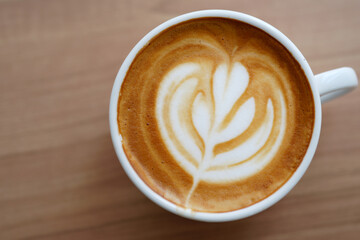 Hot coffee latte with latte art milk foam in a glass on Wooden table.