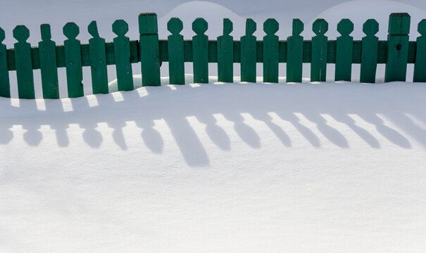 Green fence casts long shadows on fresh snow in a winter landscape 