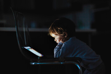 Child focused on screen in a dimly lit room at night