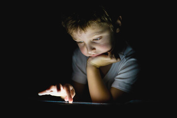Child engaged in focused activity with mobile device in darkness