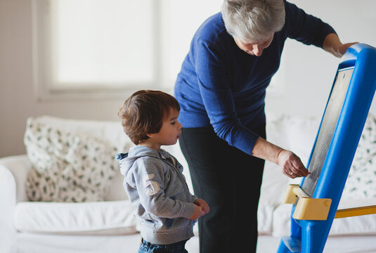 Elderly woman teaches young boy to draw on a chalkboard - Powered by Adobe