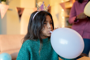 Child blowing a balloon during a festive celebration.