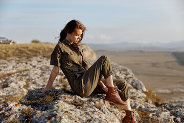 Woman sitting on top of rock in green shirt and brown boots enjoying nature beauty and tranquility...