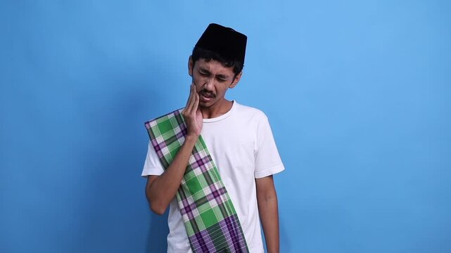 Sick ill frowning young asian muslim man touching cheek suffering from toothache in ramadan month. Healthy lifestyle concept