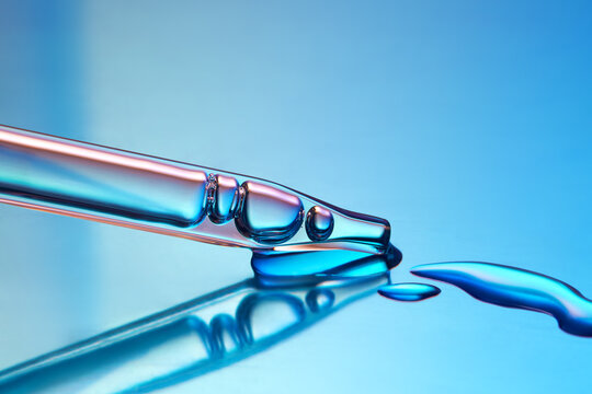 Close up of a pipette dispensing liquid on gradient blue background.