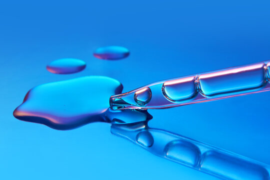 Close up of a pipette dispensing liquid on gradient blue background.