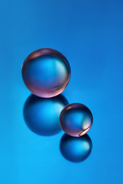 Two glass spheres on reflective gradient blue background. 