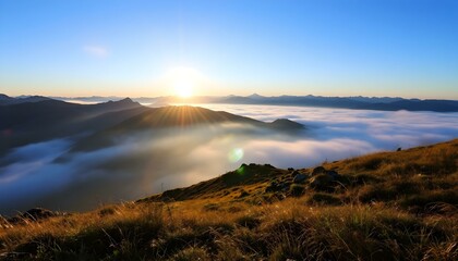 Obraz premium Sunrise over misty mountain range with golden grassy slopes, blue sky, and distant peaks fading into the horizon.