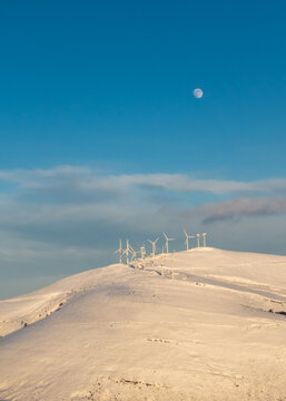  wind generators on a snow covered mountain. Big moon visible 