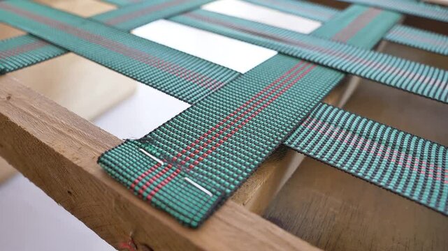 Panning motion from right to left showcasing upholstery straps neatly stapled to a wooden furniture frame. The shot highlights the craftsmanship and secure attachment of the straps
