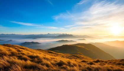Sunrise over misty mountain range with golden grassy slopes, blue sky, and distant peaks fading into the horizon.
