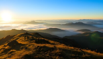 Sunrise over misty mountain range with golden grassy slopes, blue sky, and distant peaks fading into the horizon.