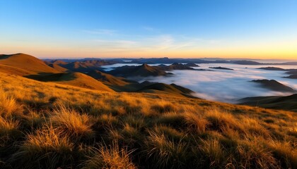 Sunrise over misty mountain range with golden grassy slopes, blue sky, and distant peaks fading into the horizon.