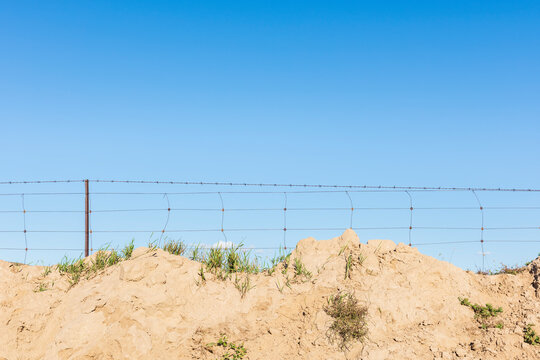 Barbed wire fence with sandy mound under a clear blue sky.