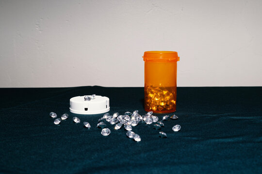 Orange pill bottle with faux diamond pills spread over fabric tabletop