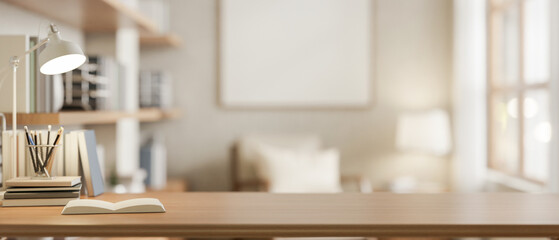 A wooden desk features a lamp, books, and stationery with a blurred background of a living room.
