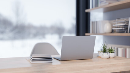 A back view of a laptop placed on a desk in a modern office with a overlooking a snowy winter view.