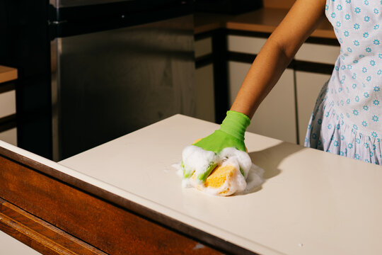 Anonymous hand cleaning a kitchen counter with green gloves