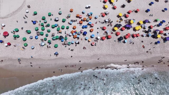 Tropical beach top down aerial view, showing people relaxing on the beautiful Copacabana Beach and coast on a bright sunny summer day. Slow motion waves crashing on the beach

