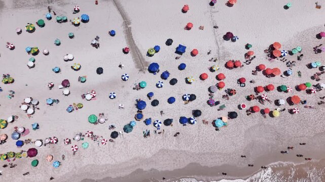 Aerial top down view showing people relaxing on the beautiful Copacabana Beach and coast on a bright sunny summer day. Slow motion drone view