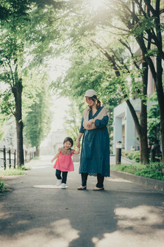 緑の小道を歩く赤ちゃんを抱っこしたお母さんと女の子