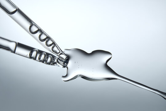 Close up of a pipette dispensing liquid on reflective gray background.