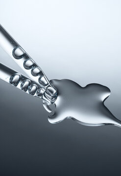 Close up of a pipette dispensing liquid on reflective gray background.