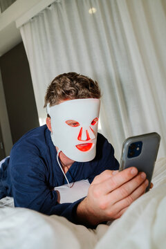Male Using Smartphone While Wearing LED Facial Mask
