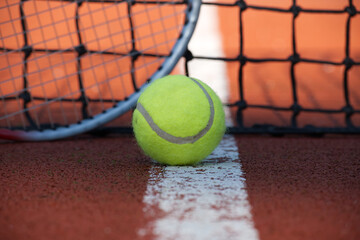 Tennis ball lying on the court next to a racket and the net
