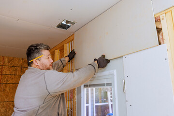 Handyman works on attaching drywall sheetrock to wall in home during renovation