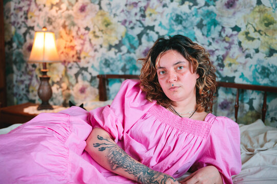 Editorial portrait of young woman on bed in pink dress 