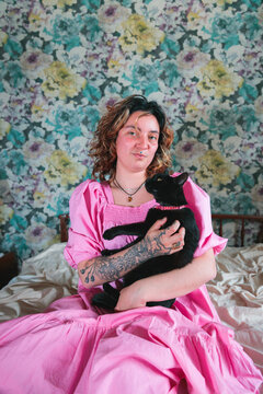 Young woman with pink dress holding black cat in bedroom